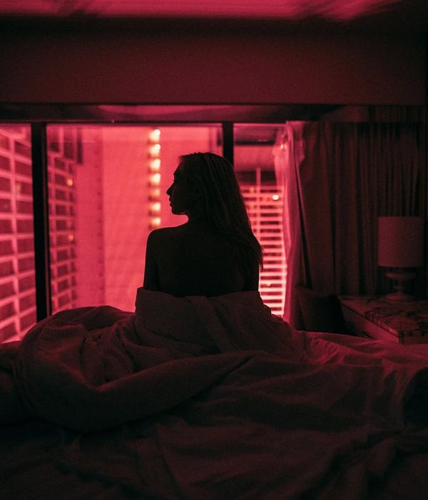 Woman in a calm, focused pose in a dark room with pink light.